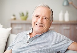 Older man smiling on the couch and following dental implant post-op instructions in Downers Grove