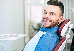 Man in denim shirt smiling in dental chair