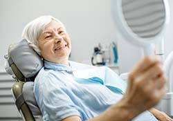 senior woman admiring her smile in a mirror after getting dental implants