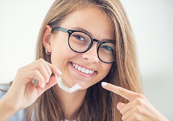 Smiling young woman pointing to her Invisalign clear aligner