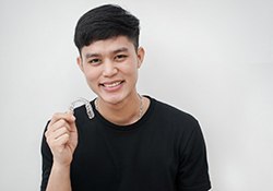 Young man in black shirt holding Invisalign clear aligner