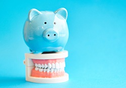 Piggy bank atop teeth representing the cost of Invisalign in Downers Grove