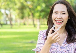 Smiling woman standing outside taking out her Invisalign