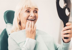 An older woman looking at her dentures in a hand mirror