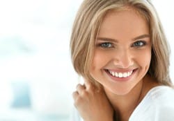 A young woman with blonde hair smiling because of the more subtle look she’s obtained from a metal-free dental crown