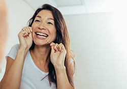 Smiling woman flossing as instructed by her Downers Grove emergency dentist 