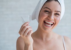 Smiling woman holding mouthguard to prevent cracked teeth in Downers Grove