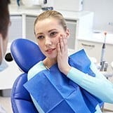 Woman in dental chair holding cheek